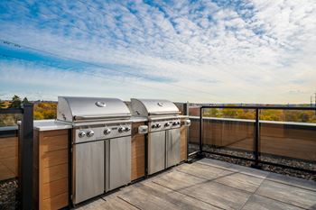 two stainless steel barbecue grills on a rooftop deck with a cloudy sky